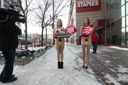 Courtney Shwetz (centre) with her cohort Emily Lavender  sell the virtues of being vegan to a passer-by by handing out free vegan pizza in only short dresses in front of Portage Place Wednesday.   See Bartley Kives story.  Dec 03,  2014 Ruth Bonneville / Winnipeg Free Press