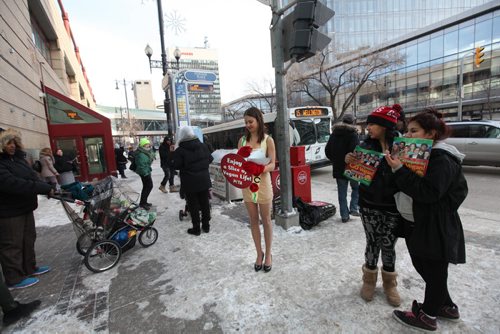 As Emily Lavender sells the virtues of being vegan on Portage Ave. over the lunch hour  by handing out free vegan pizza in only short a dress Heather Beardy (hat) and her friend Cherish Harper from Island Lake First Nation hold PETA propaganda material given to them as they look on.  See Bartley Kives story.  Dec 03,  2014 Ruth Bonneville / Winnipeg Free Press