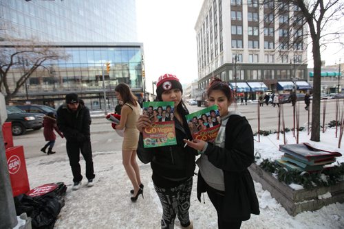 As Emily Lavender sells the virtues of being vegan on Portage Ave. over the lunch hour  by handing out free vegan pizza in only short a dress Heather Beardy (hat) and her friend Cherish Harper from Island Lake First Nation hold PETA propaganda material given to them as they look on.  See Bartley Kives story.  Dec 03,  2014 Ruth Bonneville / Winnipeg Free Press