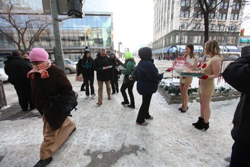 PETA employee Emily Lavender (left, brown hair) sells the virtues of being vegan to a passer-by with her cohort Courtney Shwetz (blond) by handing out free vegan pizza in only short dresses in front of Portage Place Wednesday.  A warmly dressed women makes her way into Portage Place opposite them.  See Bartley Kives story.  Dec 03,  2014 Ruth Bonneville / Winnipeg Free Press