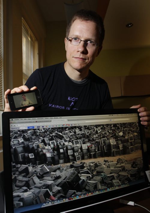 Faith Page. Rev. Tyler Gingrich at Canadian Lutheran World Relief holds his phone with an image from the video campaign called "All I want for Christmas is mining justice" (the image on the computer scene is not from this video it is a picture showing ewaste.)  Story by Brenda Suderman  Wayne Glowacki / Winnipeg Free Press Dec.5 2014