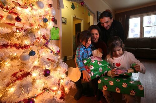 Seven-year-old Dreanna Sinclair (right, pink) and her little sister Shaelynn  - 5yrs, opens gifts they just received from Ma Mawi Wi Chi Itata Centre 12th Annual Christmas Hamper Drive which took place at R.B. Russell School Saturday morning.   Their mom Jennifer and dad Barney look on.    See story.  Dec 20,  2014 Ruth Bonneville / Winnipeg Free Press