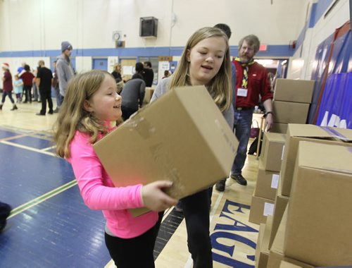 Nine-year-old Julia Lukowich gets help lifting a box from her sister Katy, 12yrs, as they box up hundreds of Christmas Hampers with many volunteers at R.B. Russell School at Ma Mawi Wi Chi Itata Centre's 12th Annual Christmas Hamper Drive Saturday.  See story.  Dec 20,  2014 Ruth Bonneville / Winnipeg Free Press