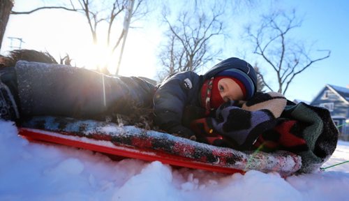 Jude Penner, 4 and a half, lays on a sled while being pulled along Westminster Avenue, by his father, James, Saturday, January 3, 2015. (TREVOR HAGAN/WINNIPEG FREE PRESS)