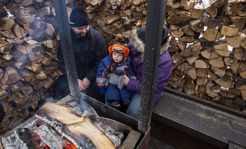 Hugh Ebbers, 18 months, warms up by the fire with his parents Craig Ebbers (left) and Megan Wilton (right) inside one of the warming huts at The Forks. Hundreds took advantage of the slightly warmer weather and headed to The Forks for the kick-off of its winter adventure programming. 150118 - Sunday, January 18, 2015 -  (MIKE DEAL / WINNIPEG FREE PRESS)