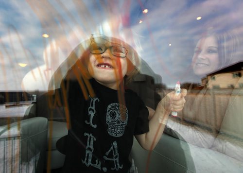 Four yr old Cian Anaka drawing on the family room window with his markers Monday, mom Kristi watches (right). See Mary Agnes story re: Child Care. January 19, 2015 - (Phil Hossack / Winipeg Free Press)