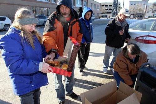 Marsha Eldridge holds up a box of doughnuts (left) while her husband Ron (right) crouches to pour a hot chocolate outside Booth Centre on Henry Avenue Sunday afternoon. Marsha and her husband Ron have been handing out hot drinks for those in need for years and today was no different, people were very happy to see them.  150201 February 01, 2015 Mike Deal / Winnipeg Free Press