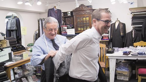 Canstar Community News Serafino Falvo assists one of his customers in putting on a custom tailored suit at his shop on Corydon.