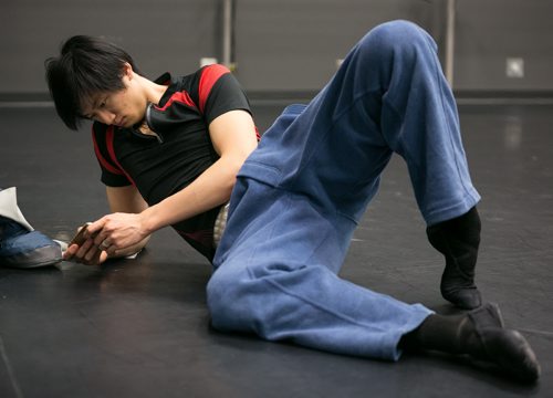 Xing stretches his hip and feet while playing a game on his phone during a break in the Swan Lake pas de deux rehearsal.  150220 - Friday, February 20, 2015 - (Melissa Tait / Winnipeg Free Press)