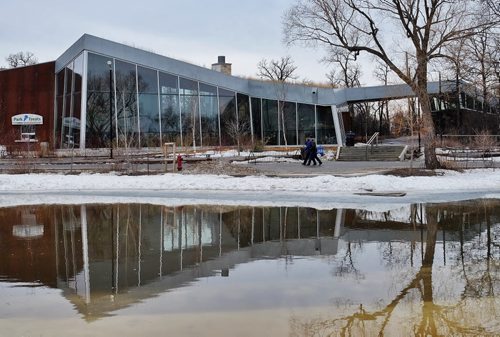 A couple walks along the Duck Pond as it casts a mirror reflection of the Qualico Family Centre at Assiniboine Park on a cool overcast Sunday morning. The high is expected to hit double digits by mid-day.  150315 March 15, 2015 Mike Deal / Winnipeg Free Press