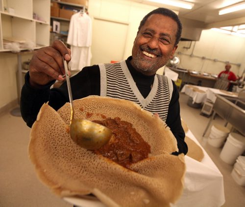 Ali Saeed dishes out a traditional Ethiopian meal of spicy lamb on Injera. He's posing in a Sargent ave bakery where they make injera- its the only bakery in Wpg that produces the special Ethiopian spongy bread for stores and restaurants. Ali is proud Canadian businessman, property owner, taxpayer and sponsor of more than 100 refugees whove settled successful here. For Sanders story on what would happen if all the newcomers who were told to go back to where they came from actually did. See Carol Sanders story. March 19, 2015 - (Phil Hossack / Winnipeg Free Press)
