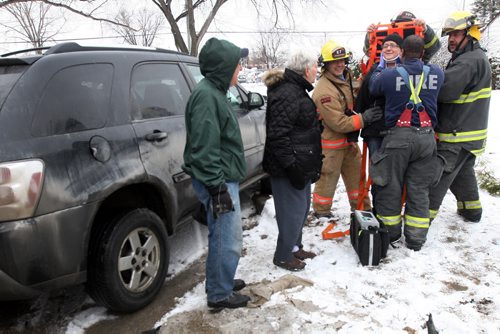 Firefighter First Responders secure a patient on a backboard at the scene of a mva on Leila Ave and Aiken St Monday morning- Two car were involved with one striking a home at the corner of the intersection-Breaking News- Mar 23 2015   (JOE BRYKSA / WINNIPEG FREE PRESS)