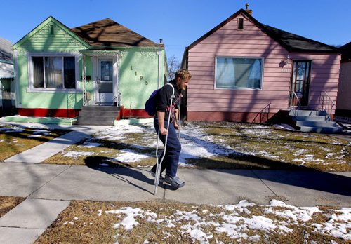 Wilfrid Reesor Taylor limps along Sherburn Street on crutches in front of two bright coloured homes. He said when he moved into the area he noticed the contrast in the homes. BORIS MINKEVICH/WINNIPEG FREE PRESS MARCH 26, 2015