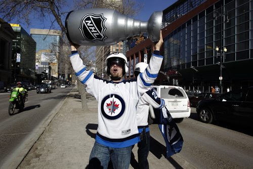 Winnipeg Jets fan Cody Laschyn lifts a blow-up Stanley Cup into the air in the centre of Portage Ave. as cars honk their horns in celebration of the Jets heading into the playoffs Saturday afternoon. His friend Tyler Macfarlane waves a Jets banner behind him.   Ruth Bonneville / Winnipeg Free Press March 26, 2015