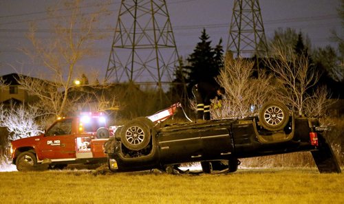 A tow truck driver works at the scene where a truck rolled over in the grass along Bishop Grandin near Lakewood Blvd, late Friday, April 24, 2015. (TREVOR HAGAN/WINNIPEG FREE PRESS)