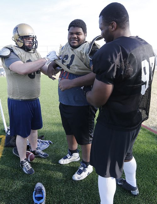 April 28, 2015 - 150427  -   Christian Kruze (L) and David Onyemata (R), from Nigeria, assist Jeffrey Otoakhia, also from Nigeria, with his new uniform before Bison practice at the University of Manitoba Tuesday, April 28, 2015. John Woods / Winnipeg Free Press