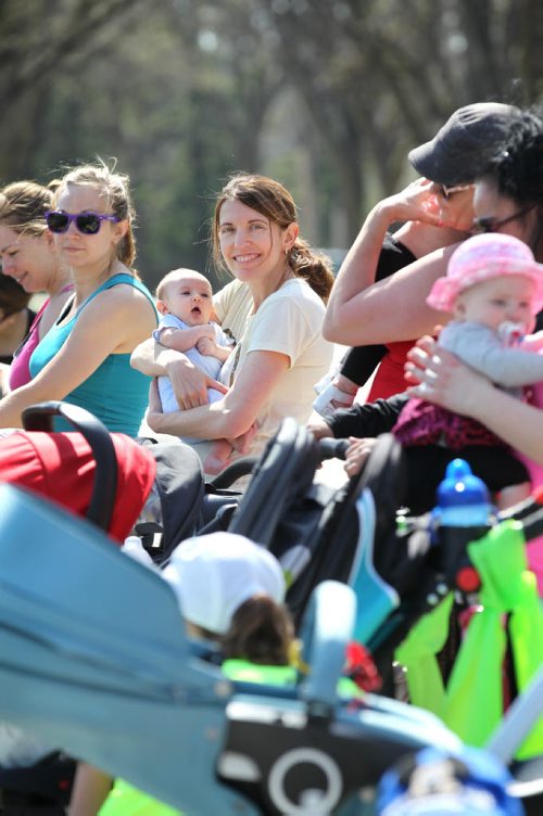 Amanda Greisman (beige shirt, smiling)  holds 2-month-old Amelia close with other moms during a short break in their workout class. See below for more info.

49.8 Certified post and pre natal trainer, Cindy Miller (front of crowd, red hair with pony tail) hosts workout sessions for new moms at Assiniboine park recently.  Classes last 45 - 50 minutes - moms walk vigorously for 5 minutes with their strollers, then pause to do lunges, step-ups, etc. for 5 minutes, then walk again, stop again until meeting back at the starting point, the pavilion, to do a cool down stretch.    See story Dave Sanderson's story. May 01, 2015 Ruth Bonneville / Winnipeg Free Press