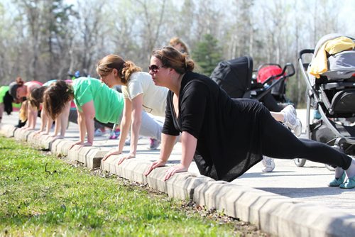 Moms hold themselves up in a plank position as part of their workout class. See below for more info.
49.8 Certified post and pre natal trainer, Cindy Miller (front of crowd, red hair with pony tail) hosts workout sessions for new moms at Assiniboine park recently.  Classes last 45 - 50 minutes - moms walk vigorously for 5 minutes with their strollers, then pause to do lunges, step-ups, etc. for 5 minutes, then walk again, stop again until meeting back at the starting point, the pavilion, to do a cool down stretch.    See story Dave Sanderson's story. May 01, 2015 Ruth Bonneville / Winnipeg Free Press