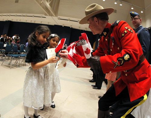 60 new Canadian Citizens today take their oath today at the Manitoba Museum. Twin girls Sarah and Lara Al-Kara, 6, left and right, get a Canadian Flag from an RCMP officer at the event. BORIS MINKEVICH/WINNIPEG FREE PRESS May 11, 2015