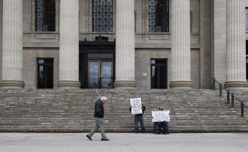 Holding signs of protest, Melvin Woodford (left) and Samuel Anderson (right) from Little Saskatchewan FN sit on the steps of the Manitoba Legislative Building Wednesday afternoon. They are two of over 350 from their First Nation that are still living as evacuees in Winnipeg from the flood of 2011.  150513 May 13, 2015 Mike Deal / Winnipeg Free Press