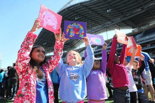 Young students from Whyte Ridge School in the Pembina Trails School Division hold their artwork up before placing it on a huge tarp-like panel in the shape of the United Nations symbol at Investors Group Field Wednesday.   All the artwork from the 13,000 students in the Pembina Trails Division will form the UN shape that will fill the grounds of the Investors Group Field over the coming days  in recognition of the human rights of children everywhere. Standup photo  May 20, 2015 Ruth Bonneville / Winnipeg Free Press