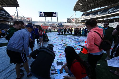 High school students the Pembina Trails School Division hold place their artwork on a huge tarp-like panel in the shape of the United Nations symbol at Investors Group Field Wednesday. All the artwork from the 13,000 students in the Pembina Trails Division will form the UN shape that will fill the grounds of the Investors Group Field over the coming days  in recognition of the human rights of children everywhere. Standup photo  May 20, 2015 Ruth Bonneville / Winnipeg Free Press