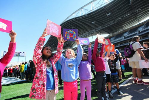 Young students from Whyte Ridge School in the Pembina Trails School Division hold their artwork up before placing it on a huge tarp-like panel in the shape of the United Nations symbol at Investors Group Field Wednesday.   All the artwork from the 13,000 students in the Pembina Trails Division will form the UN shape that will fill the grounds of the Investors Group Field over the coming days  in recognition of the human rights of children everywhere. Standup photo  May 20, 2015 Ruth Bonneville / Winnipeg Free Press