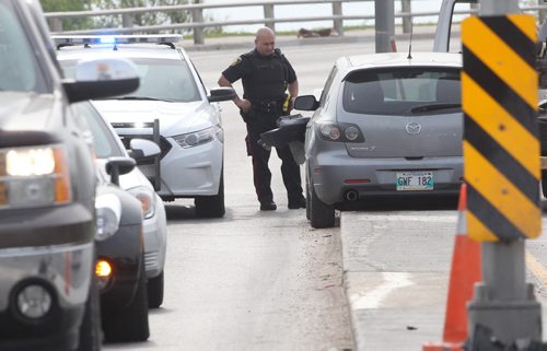 A Winnipeg Police officer checks on a car that lost control and drove on a boulevard on the Nairn overpass Monday morning near 9 AM- May 25, 2015   (JOE BRYKSA / WINNIPEG FREE PRESS)