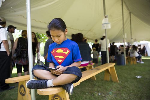 Zaine Bradburn-Anderson, seven, plays on his phone while his mom waits in line to receive their treaty cheques at the Forks in Winnipeg on Tuesday, June 9, 2015. Mikaela MacKenzie / Winnipeg Free Press