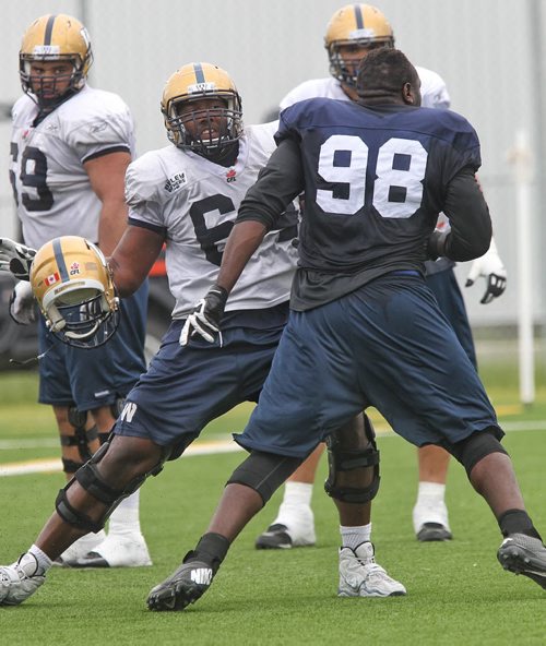 Nathaniel Collins (98) looses his helmet during practice while trying to get past Chris Greaves (64) during Winnipeg Blue Bomber practice at the soccer pitch beside Investors Group Field Sunday morning.  150614 June 14, 2015 MIKE DEAL / WINNIPEG FREE PRESS