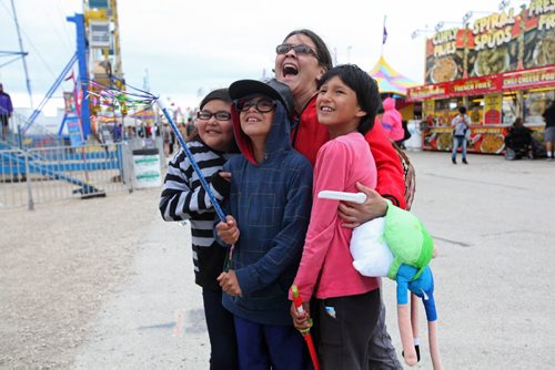 Erica Leask from Sapotaweyak Cree Nation, is all smiles as she hugs a group of kids from her reserve to keep them warm as they watch their schoolmates on a ride at the Red River Ex Wednesday evening.   June 17, 2015 Ruth Bonneville / Winnipeg Free Press