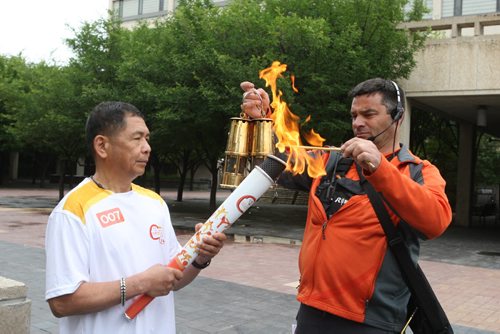 Delfin Tan is the first person that got to run with the torch from the Pan Am Games torch run. He started at City Hall in Winnipeg. Here he gets lit up by one the relay staff. BORIS MINKEVICH/WINNIPEG FREE PRESS June 22, 2015