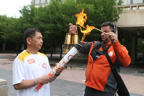 Delfin Tan is the first person that got to run with the torch from the Pan Am Games torch run. He started at City Hall in Winnipeg. Here he gets lit up by one the relay staff. BORIS MINKEVICH/WINNIPEG FREE PRESS June 22, 2015