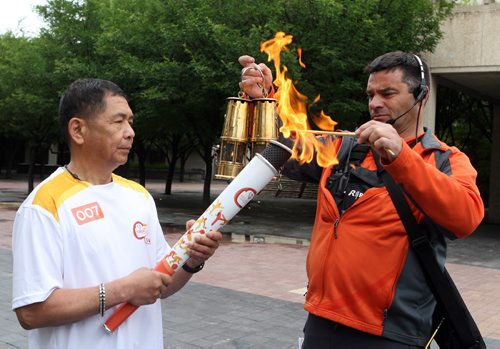LEFT- Delfin Tan is the first person that got to run with the torch from the Pan Am Games torch run. He started at City Hall in Winnipeg. Here he gets lit up by Relay Director Otto Kamenzin. BORIS MINKEVICH/WINNIPEG FREE PRESS June 22, 2015