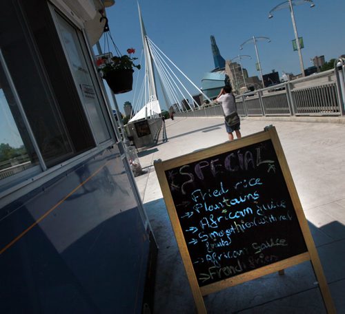 A sandwich board menu offers daily specials at Regale de l'Afrique's kiosk, one of Three seasonal kiosks designed to look like horse-drawn trams from the early 1900s open each summer on the Plaza area at the east end of the Esplanade Riel bridge. Enterprises Riel, the economic development agency for the local French community, sets the kiosks up each year for the summer. Its tourism arm operates a tourist information centre out of one, and the the other two are food kiosks. One sells house-made frozen treats and the other features African cuisine. See Murray McNeil's story. June 26, 2015 - (Phil Hossack / Winnipeg Free Press)