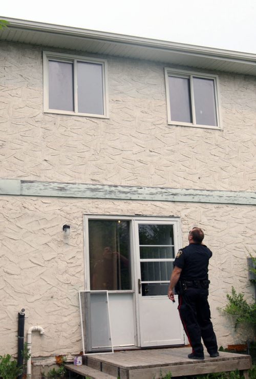 A street supervisor with the Winnipeg Police Service looks up at a second story window at a home on Ravenhill Rd were a child is reported to have fallen through the screen to the ground -Breaking News- July 02, 2015   (JOE BRYKSA / WINNIPEG FREE PRESS)