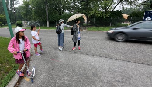 Roberta Stout, second from right, signals to oncoming traffic while walking with her friend, Lorena Fontaine, and each of their daughters, Miya Wata, 9, left, and Sarah Fontaine-Sinclair, 9.. Traffic on Wellington Crescent, which is supposed to be limited to only one block, Sunday, July 5, 2015. (TREVOR HAGAN/WINNIPEG FREE PRESS)