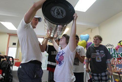 Jamie Yeo is all smiles as she gets to hold the 2015 Stanley cup over her head with the help of The Chicago Blackhawks captain and Stanley Cup champion, Jonathan Toews  during a  visit to  the Rehabilitation Centre for Children at 633 Wellington Crescent Friday.  July 10, 2015 n Ruth Bonneville / Winnipeg Free Press