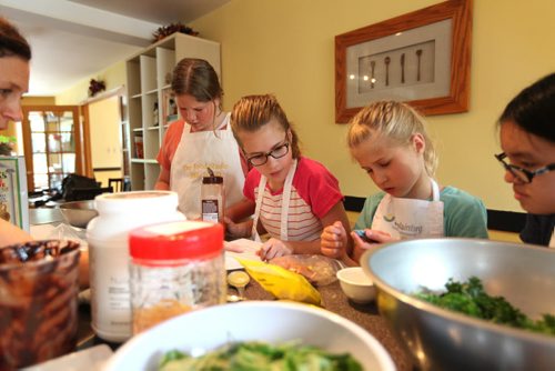 Sunday This city piece on the Food Studio, Maria Abiuis (orange shirt), owner of The Food Studio hosts cooking camps during the summer for kids & teens with the help of her sister Angela Houldsworth (grey shirt). Young chefs look at recipe to  make Kale chips during class.  See Dave Sanderson story.  July 09, 2015 Ruth Bonneville / Winnipeg Free Press