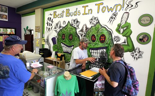 Glenn Price, the owner of Winnipeg's only medical marijuana dispensary (Your Medical Cannabis Headquarters on Main Street), says police are trying to shut him down. Officers showed up at his store earlier this week asking him to stop selling his products. Here he is in the middle behind the counter talking to a customer. On the left is Steve Koczerhan in blue. BORIS MINKEVICH/WINNIPEG FREE PRESS July 16, 2015