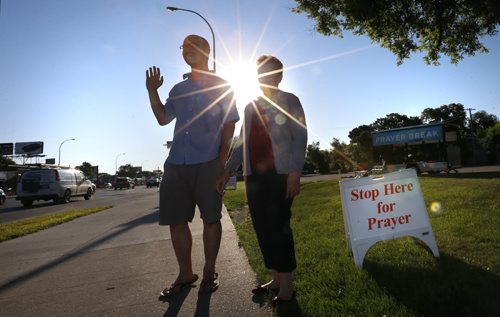 At left, Worship Minister Jeremy Penner with volunteer Ana Contreras wave and pray for commuters passing on Portage Ave. Wednesday morning in front of the Portage Avenue Church. Through out the summer church members are out 7:30 to 8:30am and 4:30 to 5:30pm on Wednesdays praying and offering a chance for commuters to stop and pray.  Brenda Suderman Faith Page  story Wayne Glowacki / Winnipeg Free Press July 22 2015