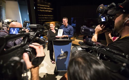 Mark Tewksbury, openly gay Olympic gold medalist, passes his medal to Canadian Museum of Human Rights interim president and CEO Gail Stephens in Winnipeg on Thursday, July 23, 2015.  Mikaela MacKenzie / Winnipeg Free Press