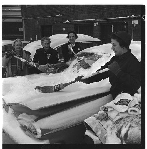 A photo of women clearing snow from a car with curling brooms was found in an envelope of negatives labeled "Snow etc. Traffic" February 13, 1962 Bill Rose / Winnipeg Free Press fparchives