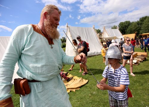 Nico Koch helps Sergey Nedelko, 9, try a helmet and sword in the Viking Village at the Gimli Icelandic Festival, Saturday, August, 8, 2015. (TREVOR HAGAN/WINNIPEG FREE PRESS)