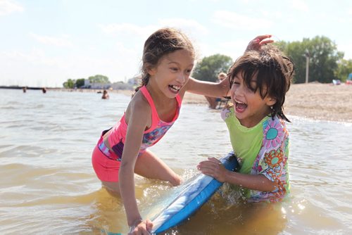 Ten-year-old Nayeli Toews and her sister Amaris - 7yrs scream as Nayeli attempts to stand on a foam surfboard while hanging onto her sister, Amaris while spending the day at Gimli beach with family Thursday.  Standup hot weather photo.   Aug 13, 2015 Ruth Bonneville / Winnipeg Free Press