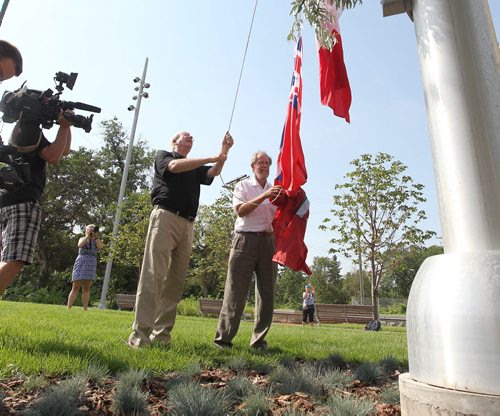 Jerry Gray (black shirt) and Garry Hilderman both with Friends of Upper Fort Garry, cut the ribbon and raise flags at the official unveiling of Upper Fort Garry  at the new provincial park on Main street Friday.   Aug 14, 2015 Ruth Bonneville / Winnipeg Free Press