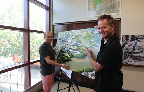 Artist Charlie Johnston (front) and Sam Katz hold photo of The Forks grounds and spot where a statue of Faron Hall will be erected on the banks of the Red River near the Esplanade Riel Bridge.  Local artist Charlie Johnston is creating the statue.   See Gordon Sinclair story.  Aug 14, 2015 Ruth Bonneville / Winnipeg Free Press
