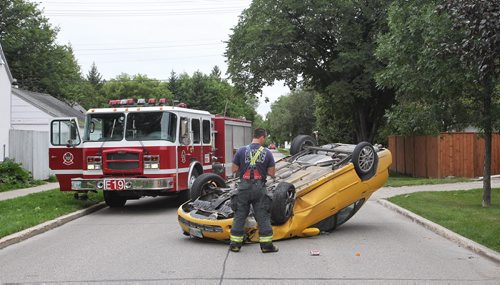 A fireman examines an upside down car early Sunday morning. The vehicle rolled over after hitting a light pole close to the intersection of Lodge Ave and Conway Street.  150816 August 16, 2015 MIKE DEAL / WINNIPEG FREE PRESS