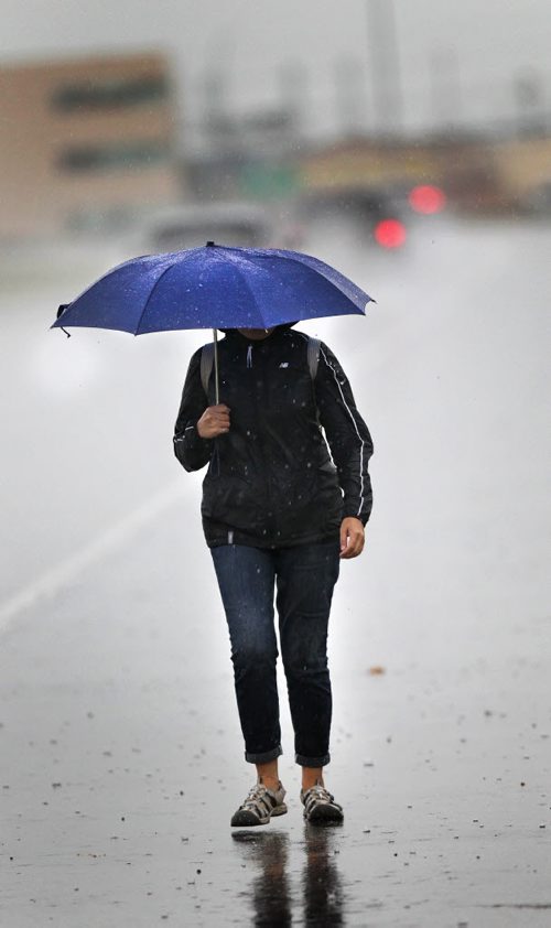 A soggy pedestrian trudges along McGillvary ave Friday afternoon after a downpour flooded streets and overpasses. A string of thunderstorms is lined up to blast the Red River Valley this afternoon and evening. September 4, 2015 - (Phil Hossack / Winnipeg Free Press)