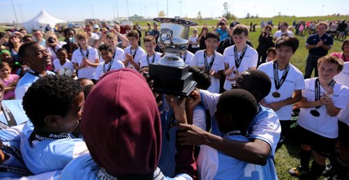 The players from IRCOM, The Immigrant and Refugee Community Organization of Manitoba Inc. soccer team, hoist their trophy as the players from St. Johns Ravenscourt look on, following the final game of the boys under 13 city recreation final at John Blumberg, Saturday, September 26, 2015. (TREVOR HAGAN/WINNIPEG FREE PRESS)